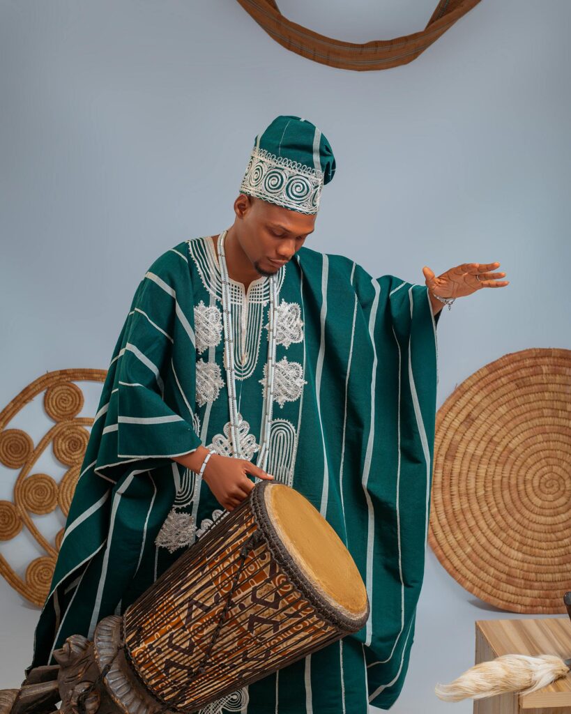Man playing a traditional drum in Nigerian attire. Cultural richness in a vibrant setting.